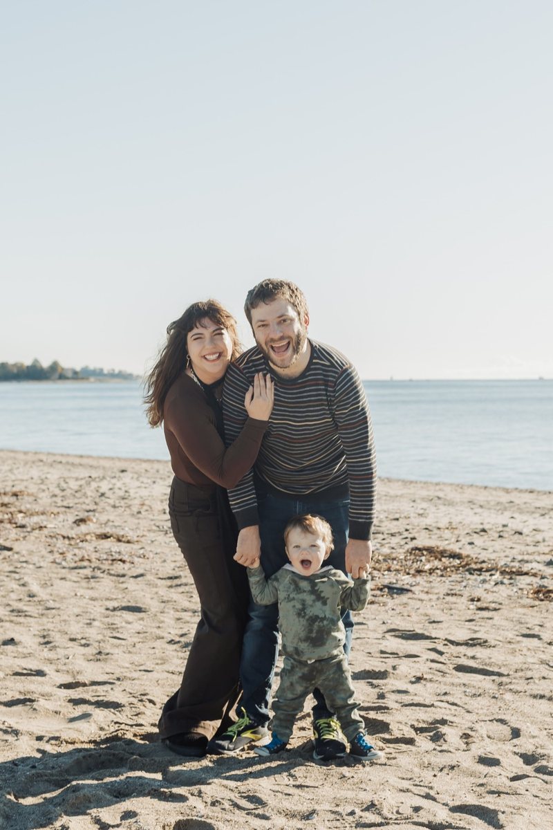 Mike with his wife and their toddler, all three laughing on a sunny beach, the toddler mid-shriek.